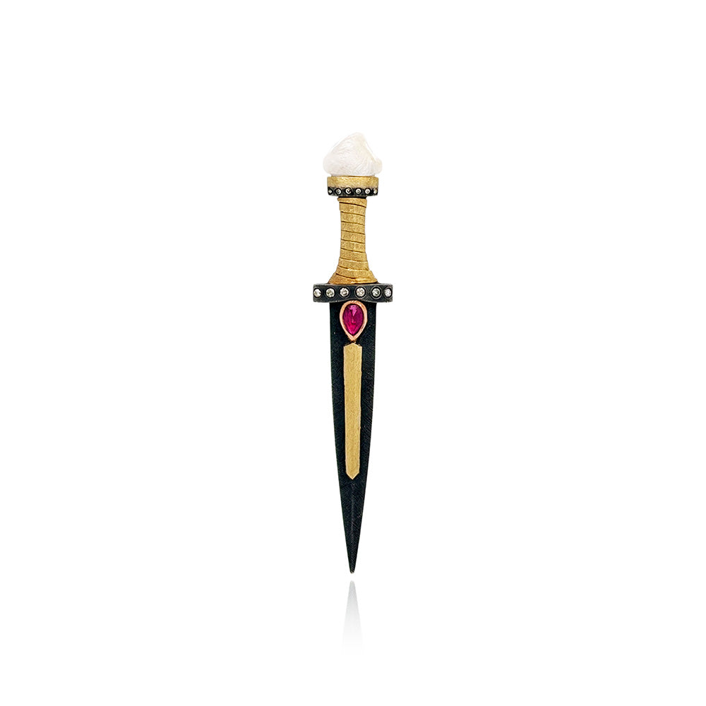 A decorative dagger-shaped pin or pendant with a black blade, gold-toned guard and center stripe, a small red heart-shaped gemstone, and a white top section, shown on a plain white background.