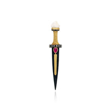 A decorative dagger-shaped pin or pendant with a black blade, gold-toned guard and center stripe, a small red heart-shaped gemstone, and a white top section, shown on a plain white background.