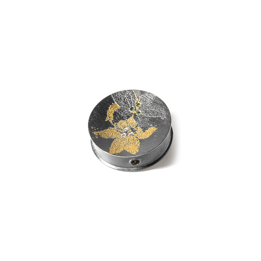 Round, double-sided "Lily" Vario clasp in oxidized sterling silver, 24k yellow gold, white (G) vs diamonds, 0.06cttw, green diamonds, 0.03cttw, and reddish-brown diamonds, 0.03cttw. Clasp is 1" in diameter.